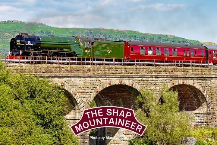 Green steam locomotive and red carriages cross an arched stone bridge, 'The Shap Mountaineer' sign in view.