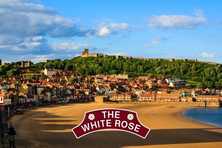 A coastal town with sandy beach, hills, and a 'The White Rose' sign in the foreground.