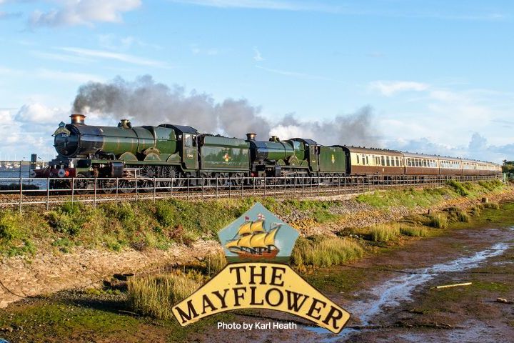 Steam train 'The Mayflower' traveling by water on a sunny day with blue sky.
