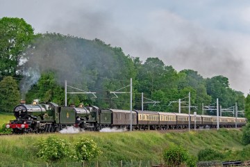 a steam engine train traveling down train tracks near a field