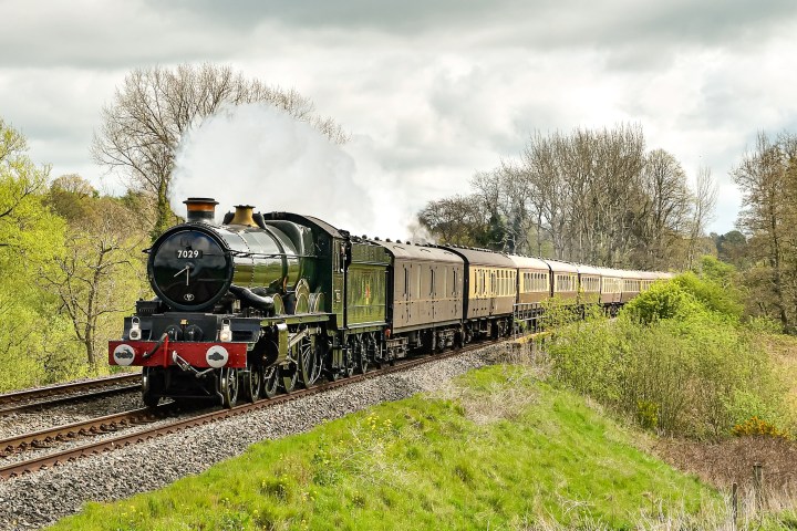 a steam engine train traveling down train tracks near a forest