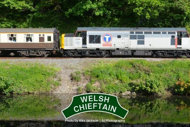 Train labeled 'Welsh Chieftain' traveling beside a river with trees in the background.