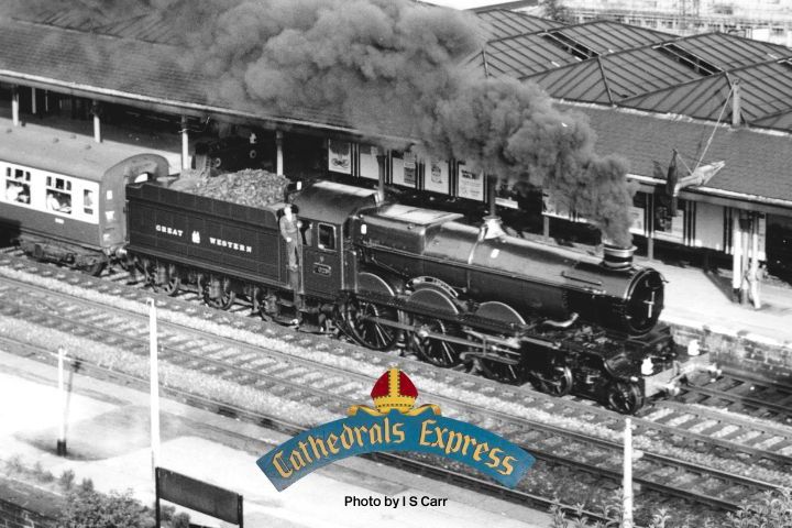 Vintage steam locomotive at station, labeled 'Cathedrals Express,' with trailing passenger cars.