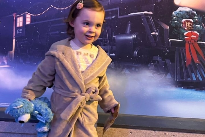Child in a robe holding a blue teddy bear in front of The Polar Express backdrop.