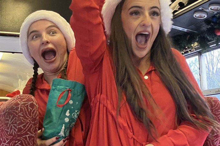 Two women in Santa hats excitedly ringing bells on a festive train.
