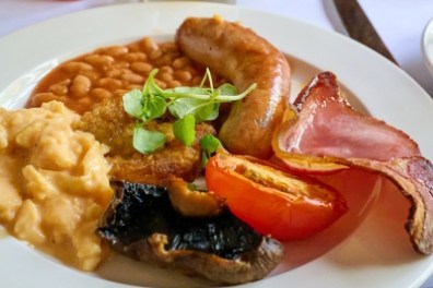 Full English breakfast with beans, sausage, bacon, egg, tomato, and mushroom on white plate.