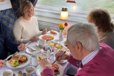 Four people enjoying breakfast at a table on a train with a scenic view.