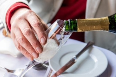 Person pouring champagne into a glass at a table setting.