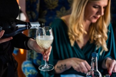 Person pouring white wine for a woman dining at a table.
