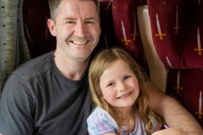 Man and young girl smiling on a train with red seats.