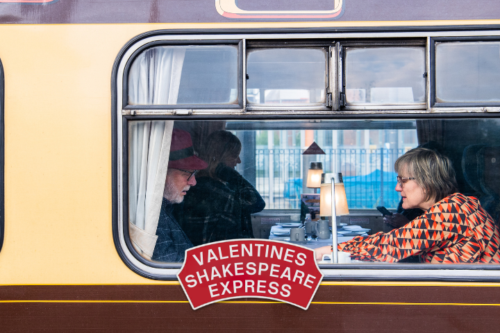 People dining on a vintage train, labeled 'Valentines Shakespeare Express'.