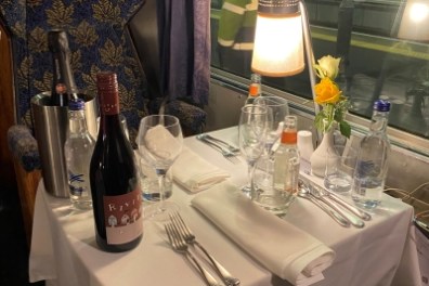 Elegant train table setting with wine, water, and a yellow rose by the window labeled 'Vintage Trains.'