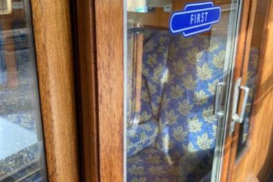 Train first-class compartment with wooden interior and blue floral seats.