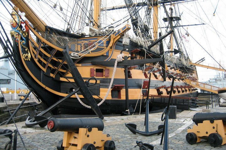 Historic ship with cannons and anchors on display at a dock.