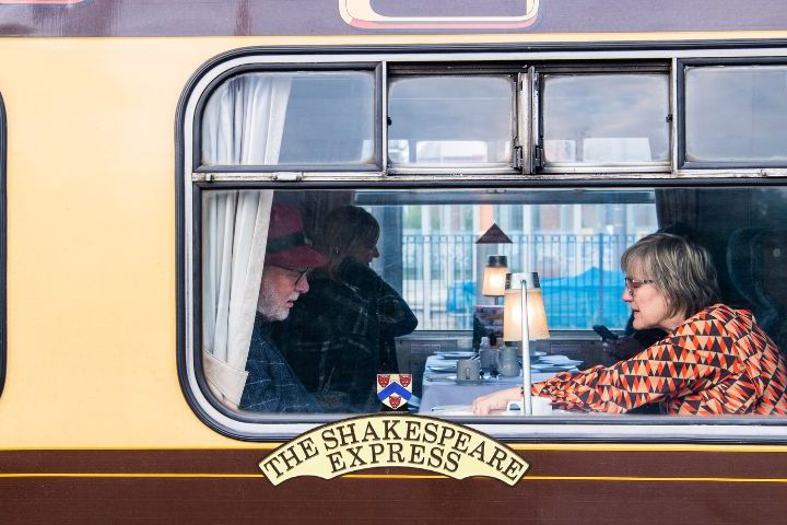 People dining inside a train carriage labeled 'The Shakespeare Express.'