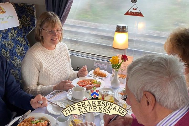 Four people dining on a train called 'The Shakespeare Express' with table set for breakfast.
