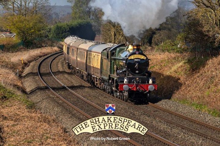 Steam train on curved tracks in rural landscape with trees and clear sky.