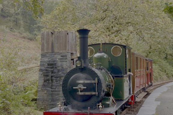 Old steam train on a track with trees and hills in the background.