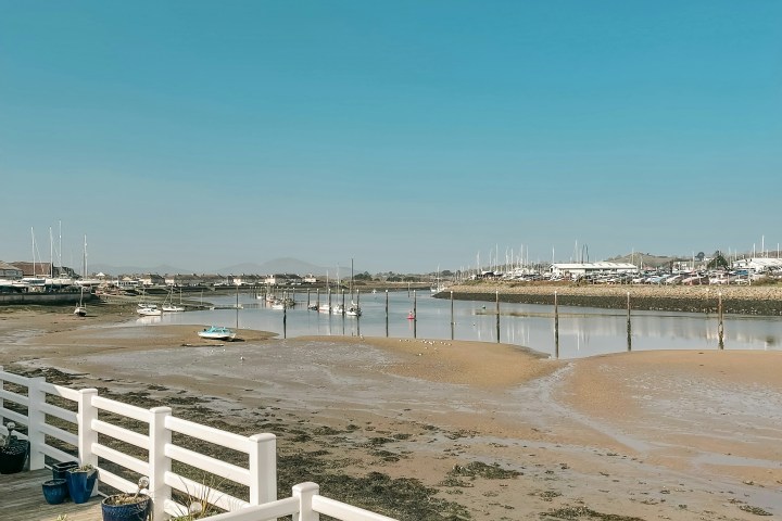 Marina view with boats, sandbar, and white fence under a clear blue sky.