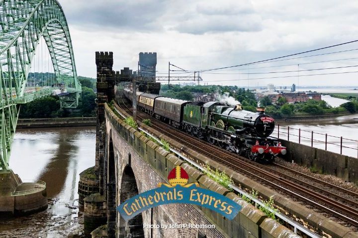 Steam train crosses a bridge next to a large green arch bridge over a wide river.