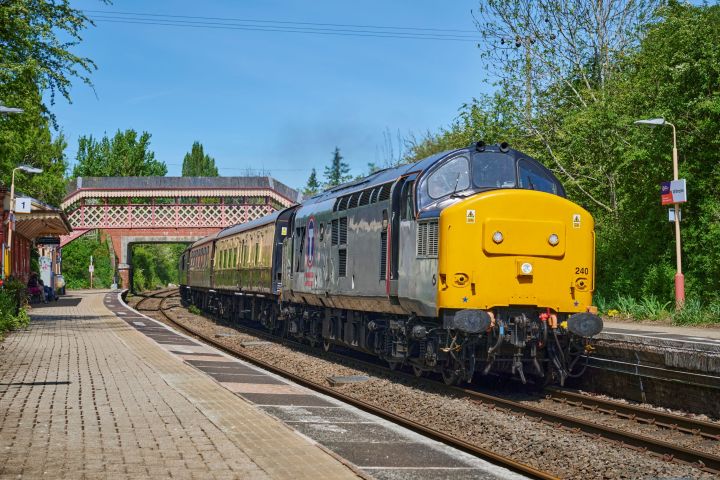 Yellow and gray train at rural train station with bridge.