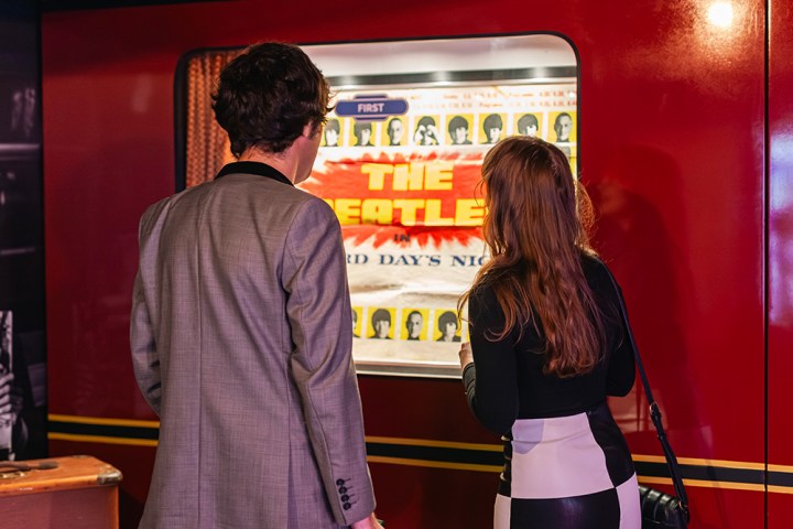 Two people view a Beatles display in a red booth.
