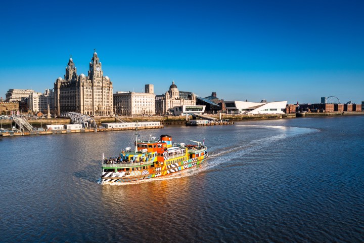Colorful ferry on a river with cityscape and clear blue sky.